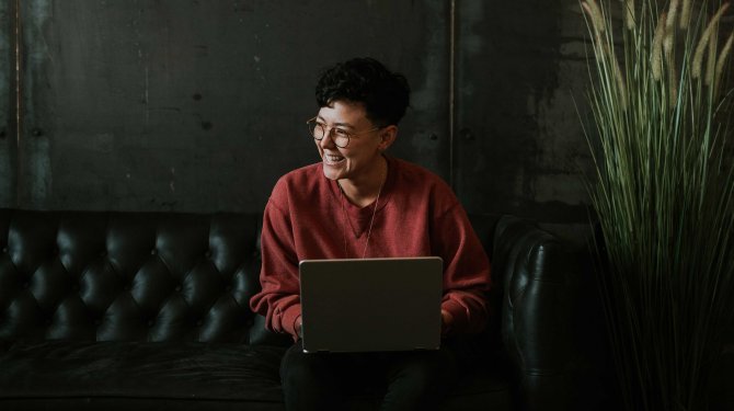 Mujer feliz sentada en un sofá con un ordenador portátil