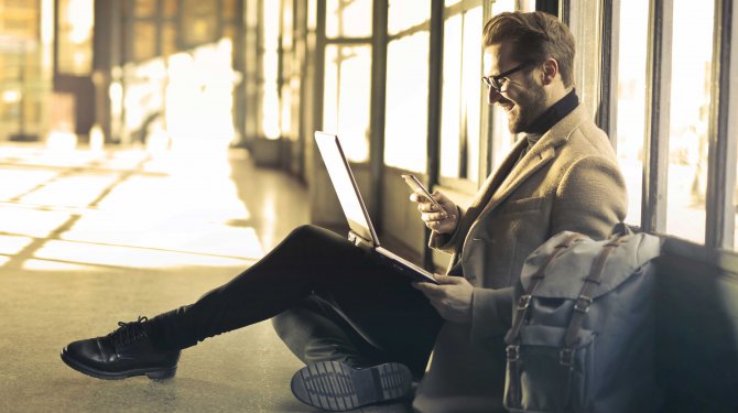 Arbeitender Mann mit Laptop und Smartphone sitz auf Boden mit optimaler Reichweite